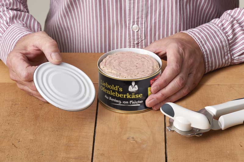 Mann mit einer frisch geöffneten Dose Leberkäse und einem Dosenöffner auf dem Tisch